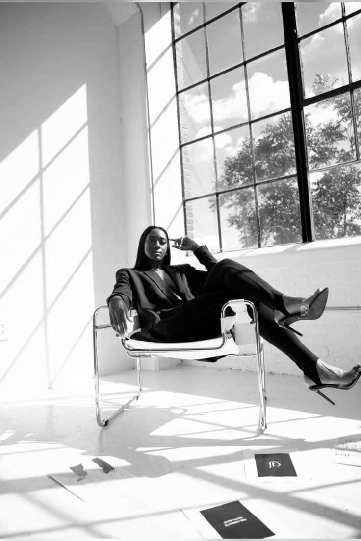 Woman in a black suit seated in a sunlit loft